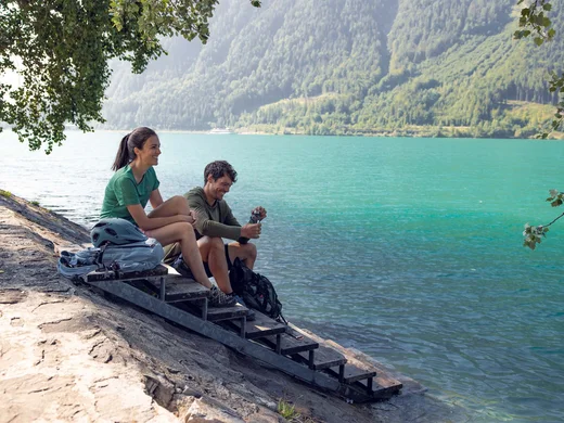 Wanderhotel Tirol: durchs Karwendel wandern und biken Zwei Personen sitzen am Seeufer mit Bergen im Hintergrund und genießen die Natur