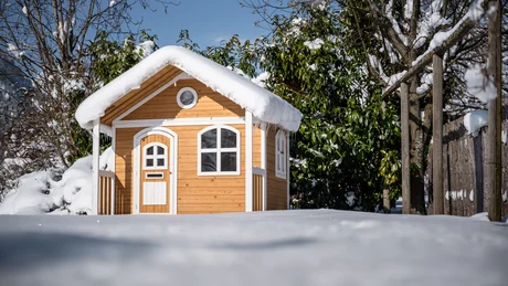 Kleines Holzhaus mit schneebedecktem Dach im Winter