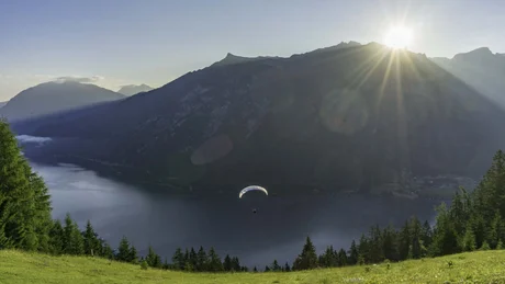 Paraglider über einem See mit Bergen und Sonne am Himmel