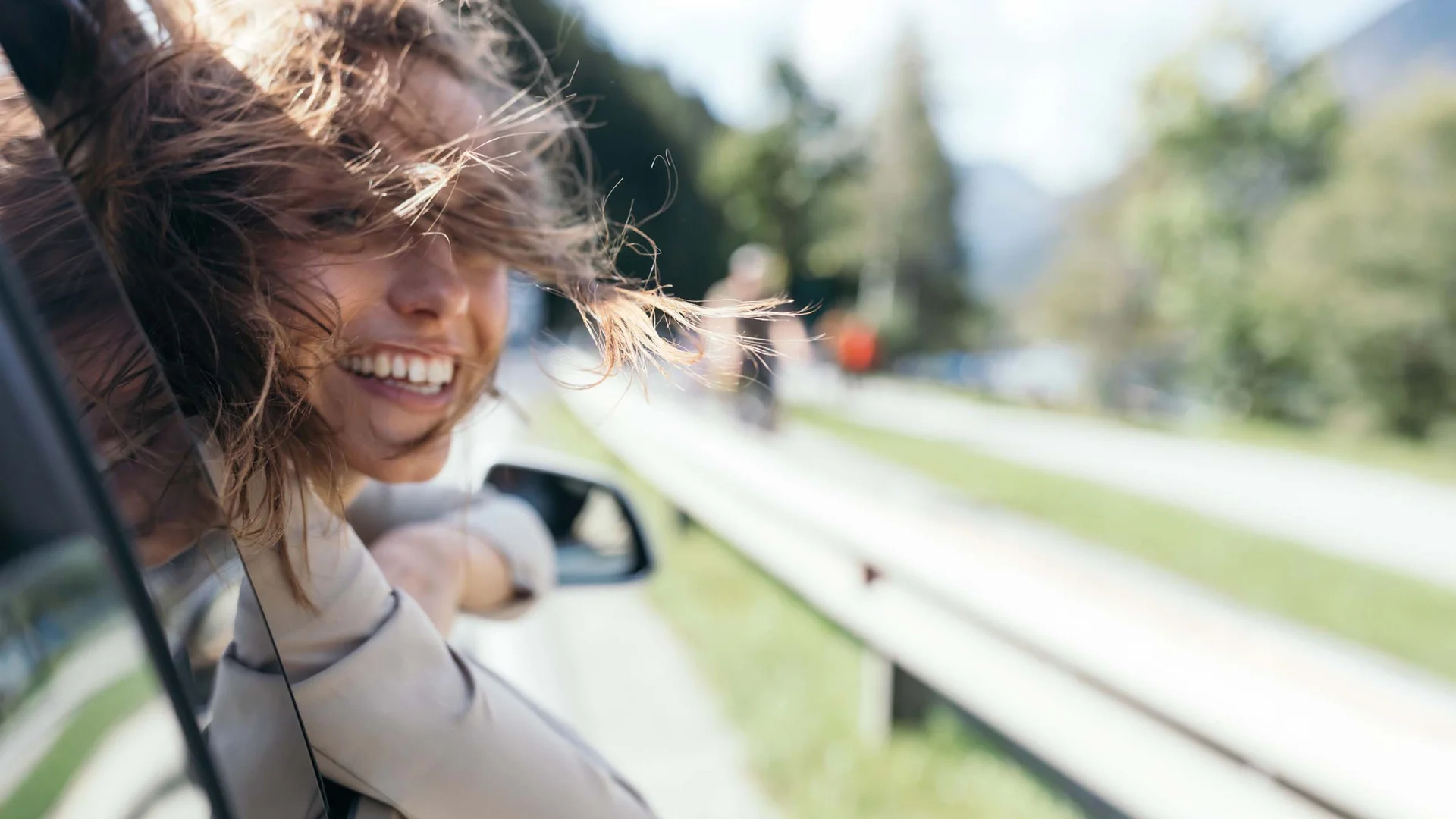 Von eurem Zuhause zu uns in den Wiesenhof Frau lehnt lächelnd aus dem Autofenster mit wehenden Haaren während der Fahrt