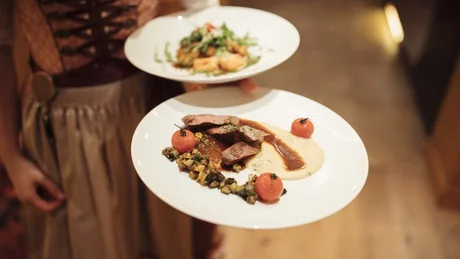 Kellnerin serviert zwei Teller mit Gourmetessen in traditioneller Tracht