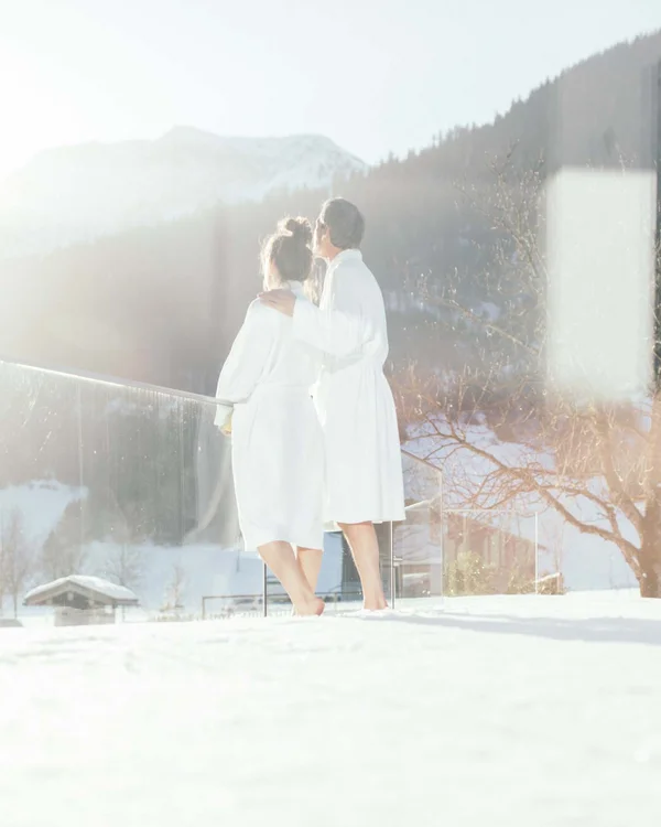 Paar in Bademänteln genießt sonnige Winterlandschaft auf Balkon
