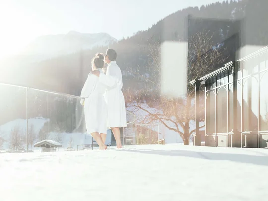 Das 4-Sterne-Hotel am Achensee: der Wiesenhof Paar in Bademänteln genießt sonnige Winterlandschaft auf Balkon