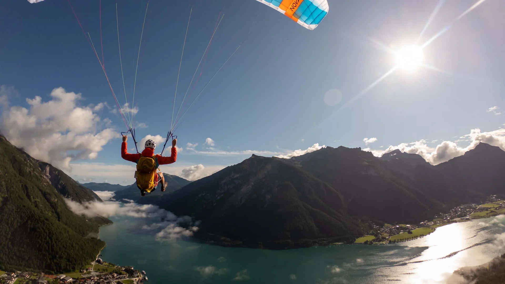 Sehenswürdigkeiten am Achensee rund um den Wiesenhof Person beim Paragliding über Bergsee mit Sonne und Wolken