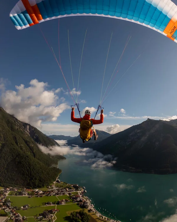 Wanderhotel Tirol: durchs Karwendel wandern und biken Person beim Paragliding über Bergsee mit Sonne und Wolken