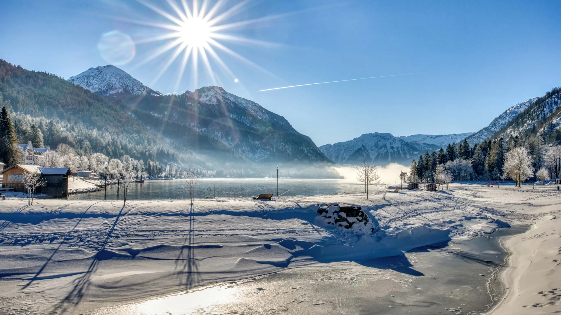 Verschneite Landschaft mit Bergen, gefrorenem See und strahlender Wintersonne