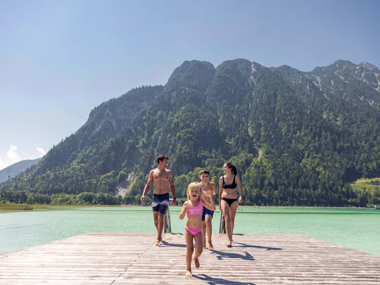 Euer Familienhotel am Achensee Familie läuft auf einem Steg am See vor bewaldeten Bergen im Sommer