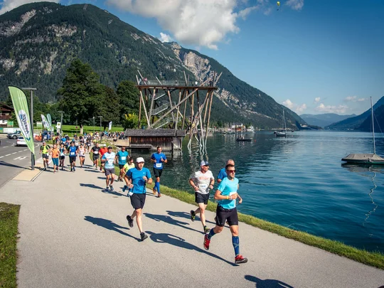 Läufer bei einem Rennen entlang eines Sees mit Bergen im Hintergrund