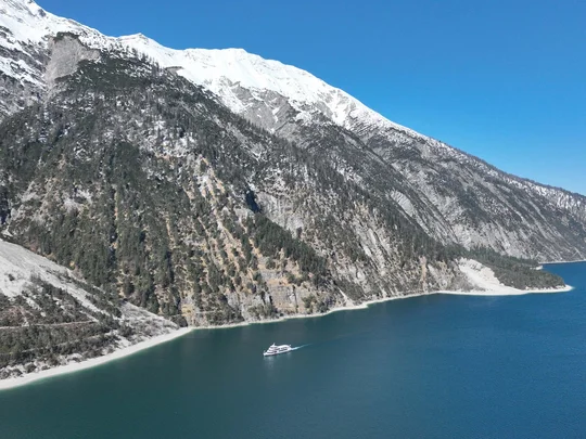 In, auf und rund um den Achensee Schneebedeckte Berge über einem blauen See mit einem weißen Boot