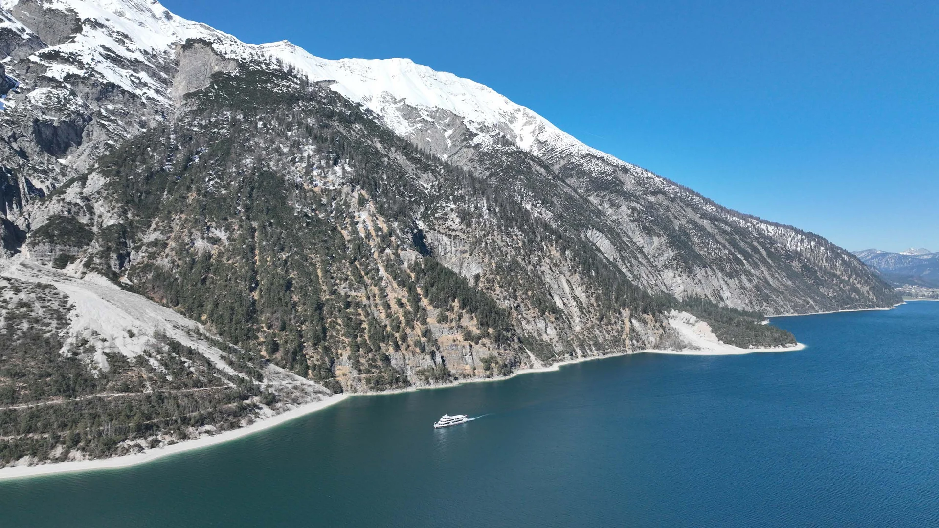 In, auf und rund um den Achensee Schneebedeckte Berge über einem blauen See mit einem weißen Boot