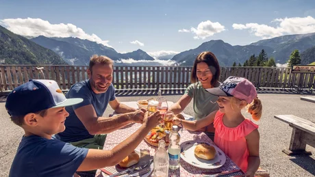 Familie stößt bei Mahlzeit mit Bergkulisse im Hintergrund an