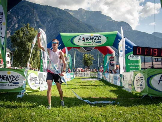 Läufer überquert Zieleinlauf eines Berglaufs mit Bergen im Hintergrund