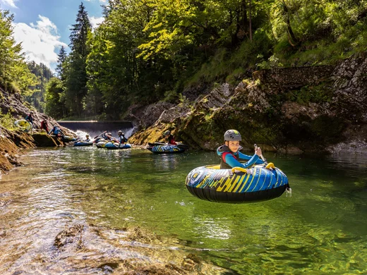 Euer Familienhotel am Achensee Kinder beim Flusstubing in einem klaren Fluss mit Helm und Schwimmweste