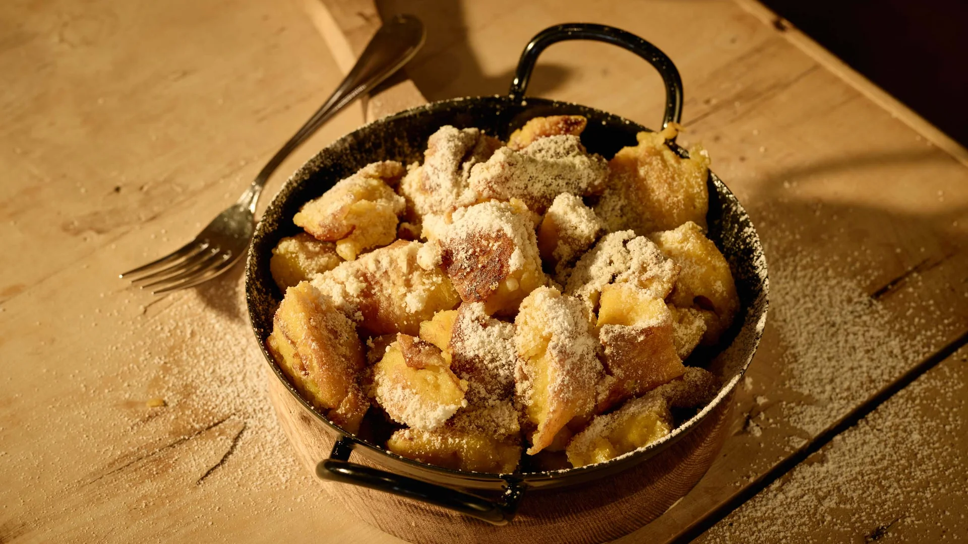Das 4-Sterne-Hotel am Achensee: der Wiesenhof Kaiserschmarrn in einer Pfanne mit Puderzucker bestreut auf Holzuntergrund