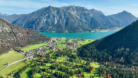 Blick auf See und Bergdorf umgeben von Wäldern und Bergen