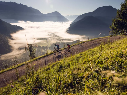 Den Achensee entdecken Zwei Mountainbiker unterwegs auf einem Bergweg mit Nebel im Tal