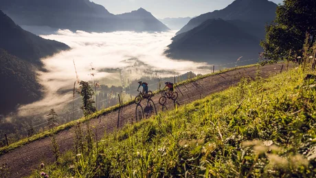 Zwei Mountainbiker unterwegs auf einem Bergweg mit Nebel im Tal
