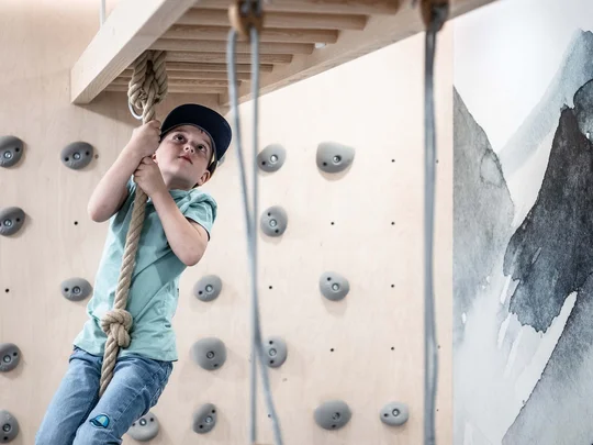 Euer Familienhotel am Achensee Kind klettert an Seil in Indoor-Kletterhalle mit Spielringen und Kletterwand