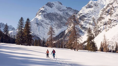 Zwei Skifahrer wandern im verschneiten Gebirge mit Tannenbäumen und blauem Himmel