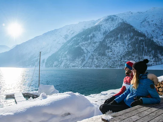 Wanderhotel Tirol: durchs Karwendel wandern und biken Paar sitzt im Winter an einem See mit verschneiten Bergen bei Sonnenschein