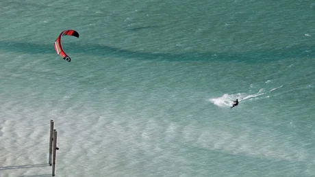 Kitesurfer mit rotem Kite auf blauem Wasser bei sonnigem Wetter