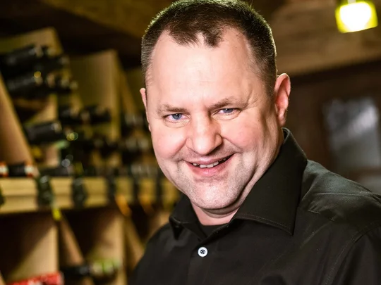 Arbeiten im Wiesenhof Mann im WIESENHOF Hemd hält eine Weinflasche in einem Weinkeller