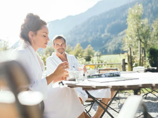 Auf in ein romantisches Hotel in Tirol Zwei Personen in Bademänteln genießen Kaffee draußen mit Bergblick