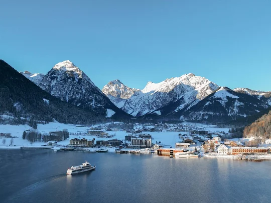 In, auf und rund um den Achensee Winterlandschaft mit verschneiten Bergen, See und Boot vor einem Dorf