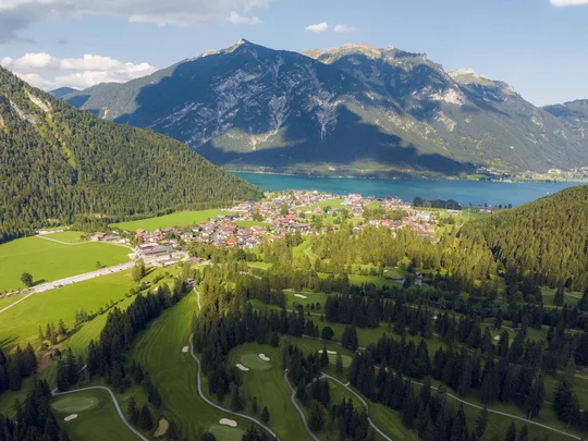 Euer Golfhotel am Achensee Luftaufnahme eines kleinen Dorfes am See zwischen bewaldeten Bergen und Golfplatz