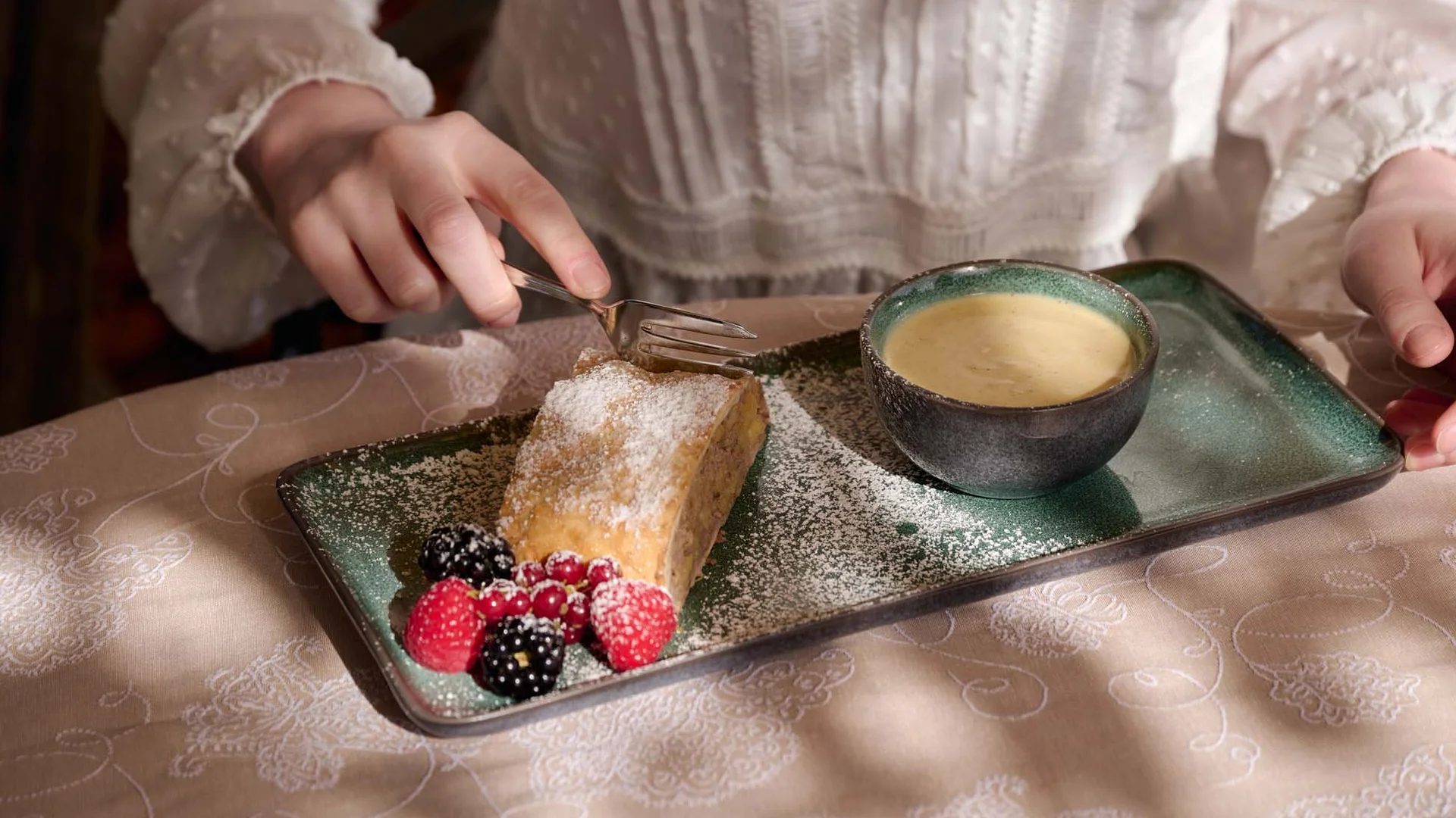 Das 4-Sterne-Hotel am Achensee: der Wiesenhof Person mit weißer Bluse isst Kuchen mit Beeren und Kaffee auf grünem Teller