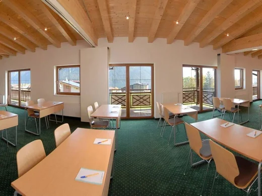 Seminarräume Achensee | Tagungshotel Wiesenhof Tirol Leerer Seminarraum mit Tischen, Stühlen, Schreibmaterial und Blick auf Berge