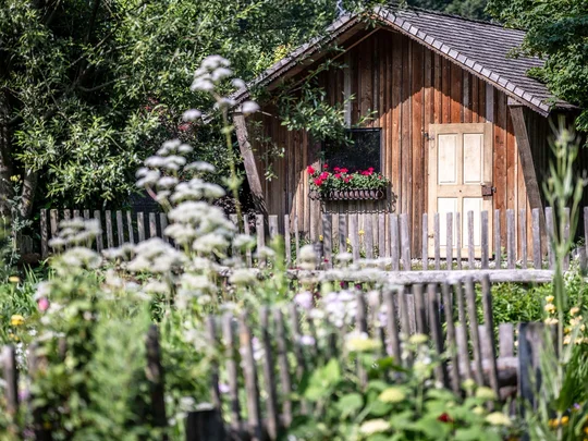 Der Wiesenhof in Pertisau und die Familie Entner mit Team Kleines Holzhaus mit Blumenkasten hinter einem Holzzaun und Blumen im Garten