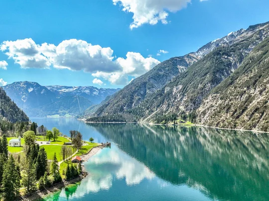 In, auf und rund um den Achensee Bergsee mit bewaldeten Hängen und wolkigem Himmel im sonnigen Frühling