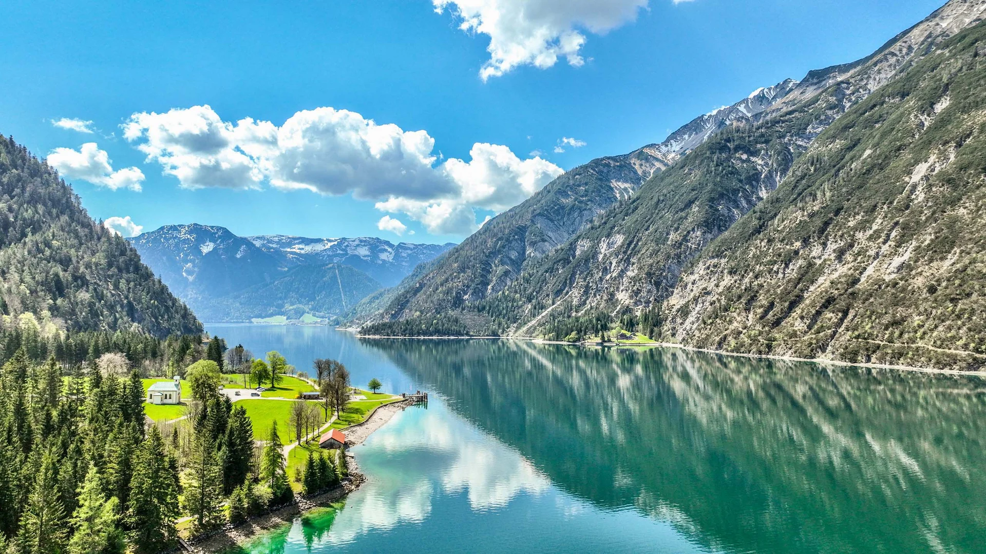 Sehenswürdigkeiten am Achensee rund um den Wiesenhof Bergsee mit bewaldeten Hängen und wolkigem Himmel im sonnigen Frühling