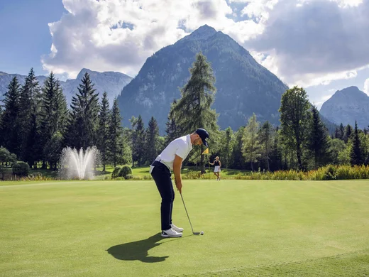 Den Achensee entdecken Mann puttet auf Golfplatz mit Bergen und Springbrunnen im Hintergrund