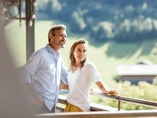 Zimmer und Suiten im Wiesenhof lächelndes Paar steht auf Balkon mit Blick auf grüne Landschaft