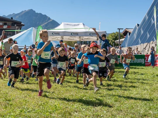 Kinder starten ein Rennen auf einer Wiese bei sonnigem Wetter in den Bergen