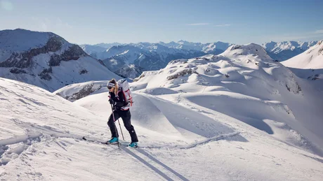 Skibergsteigerin steigt sonnigen, schneebedeckten Berg mit Alpen im Hintergrund hinauf