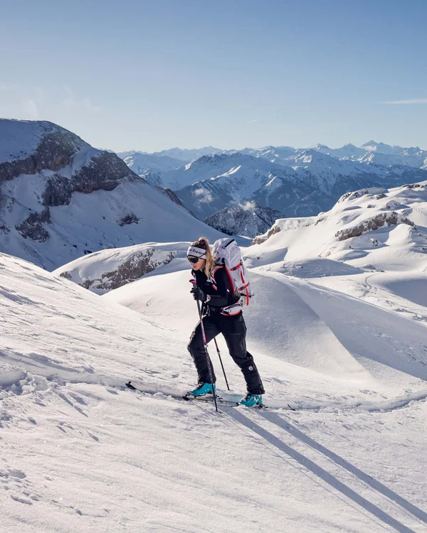 Wanderhotel Tirol: durchs Karwendel wandern und biken Skibergsteigerin steigt sonnigen, schneebedeckten Berg mit Alpen im Hintergrund hinauf
