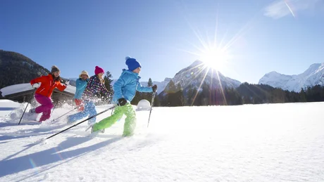 Kinder beim Skilanglauf in verschneiter Berglandschaft unter sonnigem Himmel