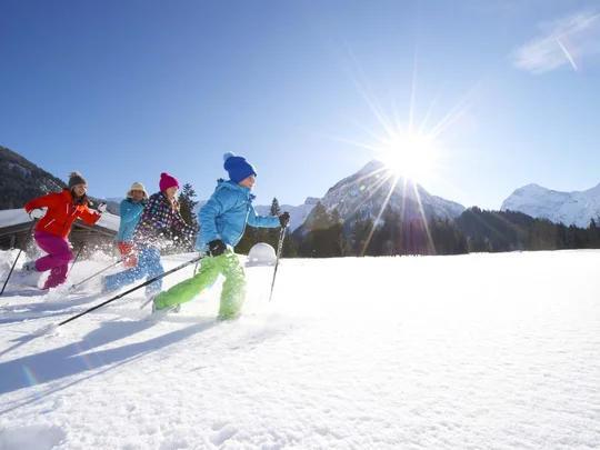 Euer Familienhotel am Achensee Kinder beim Skilanglauf in verschneiter Berglandschaft unter sonnigem Himmel