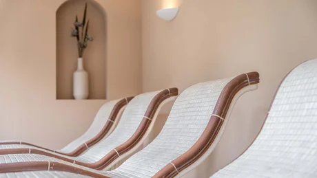 Vier weiße Lounge-Stühle mit braunen Akzenten vor beiger Wand mit Vase