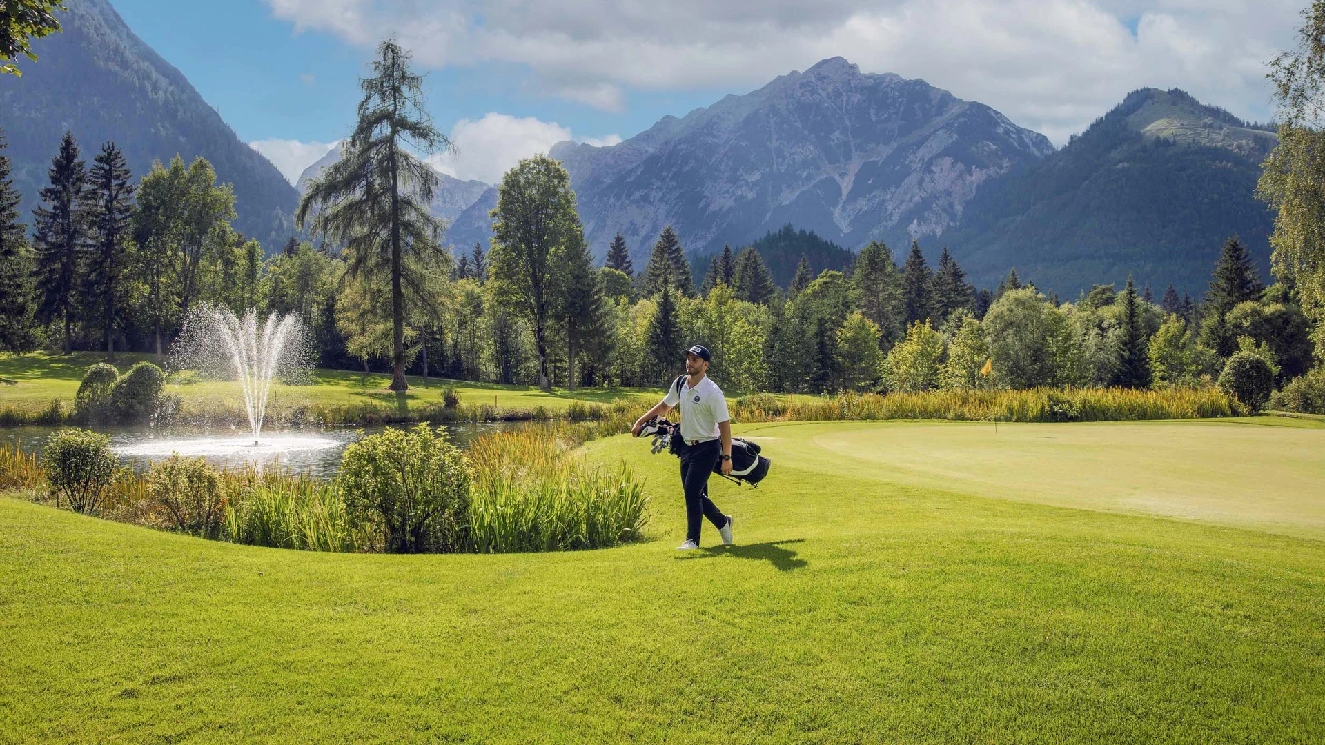 Euer Golfhotel am Achensee Golfer auf grünem Golfplatz mit Bergpanorama und Springbrunnen im Hintergrund