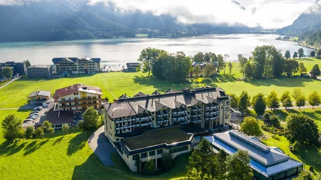Luftaufnahme eines Hotels am See mit Bergen und bewölktem Himmel im Hintergrund
