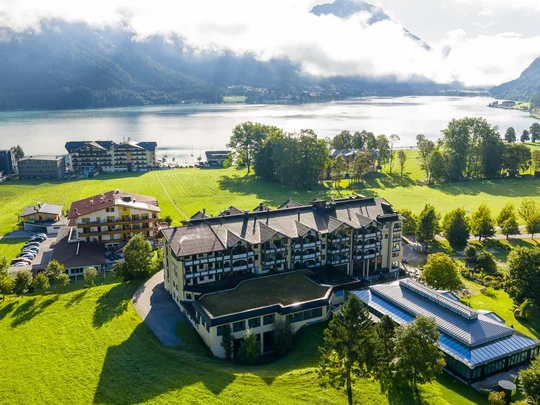Luftaufnahme eines Hotels am See mit Bergen und bewölktem Himmel im Hintergrund