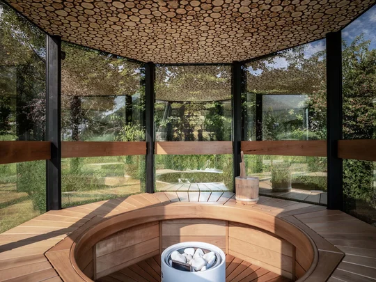 Auf in ein romantisches Hotel in Tirol Moderner Holzsauna-Innenraum mit Glaswänden und Holzdecke mit Rundstamm-Dekor