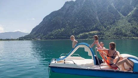 Familie auf Tretboot mit Rutsche auf Bergsee an sonnigem Tag
