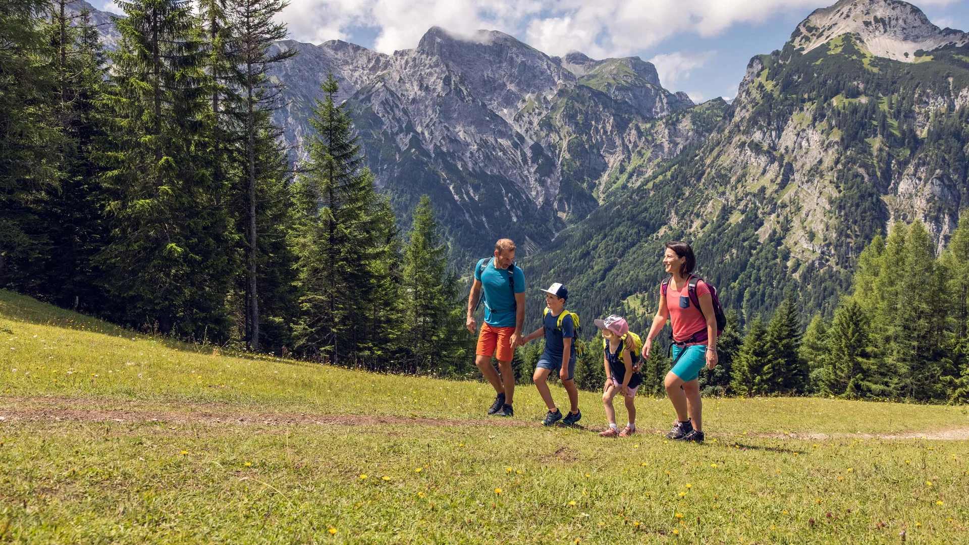 Familie wandert auf einem Pfad in den Bergen mit Tannenbäumen und blauem Himmel