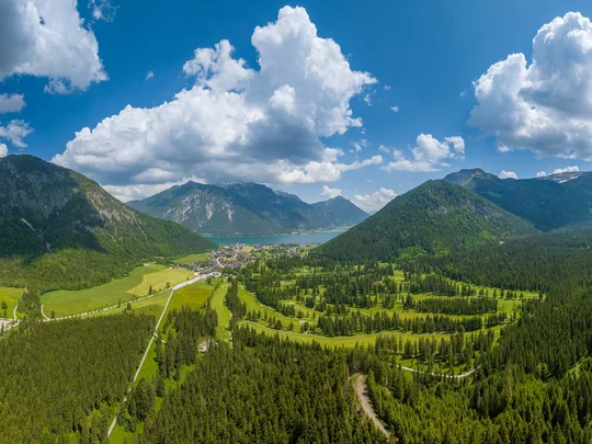 Euer Golfhotel am Achensee Panorama der Alpen mit einem See, Wäldern und einem Dorf unter blauem Himmel mit Wolken