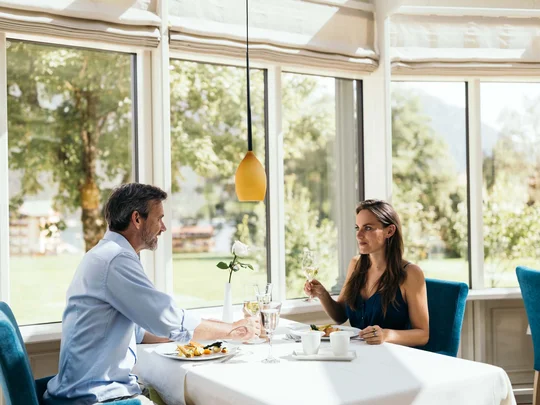 Paar beim Mittagessen in einem hellen Restaurant mit großen Fenstern und Naturblick